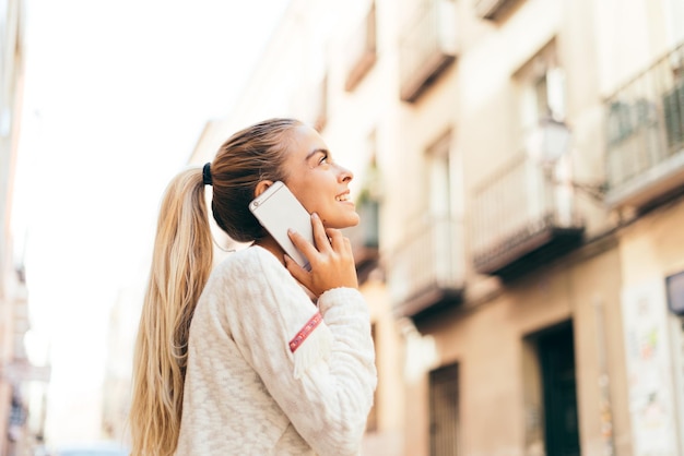 Blonde Frau, die draußen telefoniert. Junge blonde Frau, die mit dem Handy auf der Straße steht.