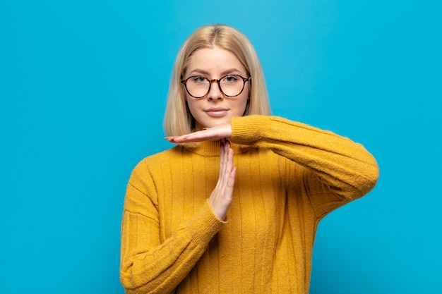 Blonde Frau, die ernst, streng, wütend und unzufrieden aussieht und Auszeitzeichen macht