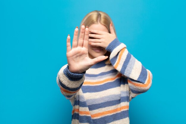 Blonde Frau, die Gesicht mit Hand bedeckt und andere Hand vorne legt und Fotos oder Bilder ablehnt