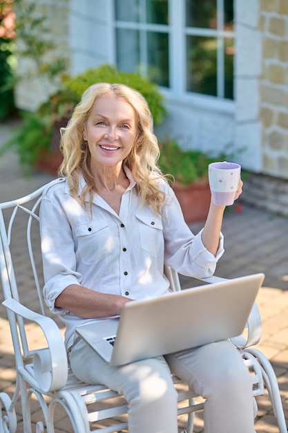 Blonde Frau, die im Internet surft, während sie ihren Morgenkaffee trinkt