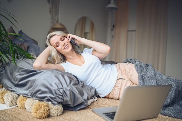 Blonde Frau, die im Schlafzimmer am Telefon spricht