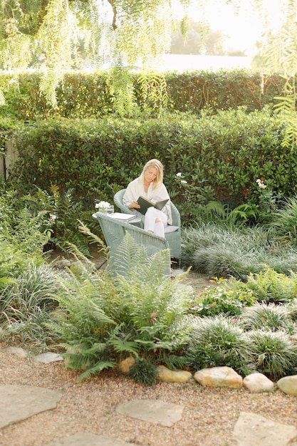 Foto blonde frau, die in einem korbstuhl in einer gartenlesung sitzt