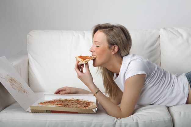 Blonde Frau, die Pizza auf der Couch isst