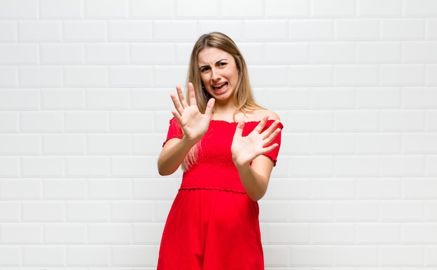 Blonde Frau, die sich erschrocken fühlt, sich zurückzieht und vor Entsetzen und Panik schreit und auf einen Albtraum reagiert