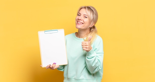 Blonde Frau, die sich stolz, sorglos, selbstbewusst und glücklich fühlt und positiv mit Daumen nach oben lächelt