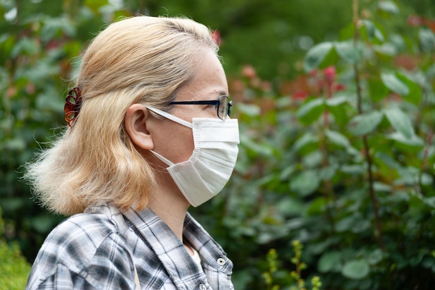 Blonde Frau gemischter Abstammung mittleren Alters mit Brille und weißer OP-Maske