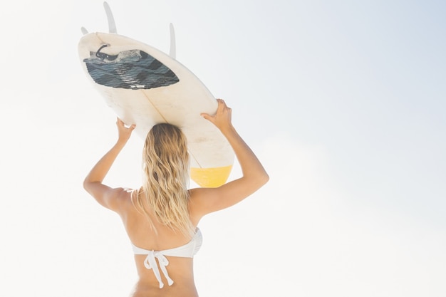 Blonde Frau hält Surfbrett über Kopf