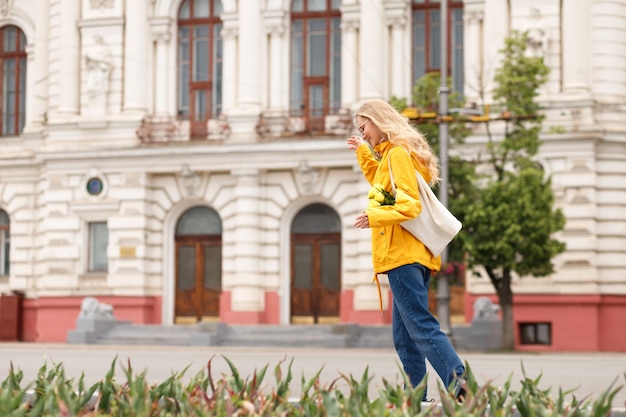 Blonde Frau im gelben Regenmantel spaziert durch die Stadt