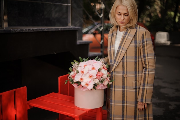 Blonde Frau im karierten Herbstmantel mit einer rosa Schachtel der Blumen