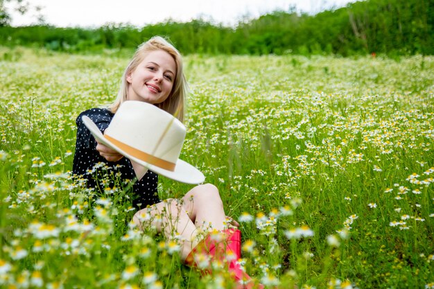 Blonde Frau im schwarzen Kleid sitzt im ländlichen Kamillenblumenfeld