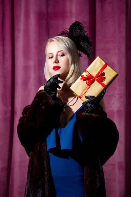 Blonde Frau im Vintage blauen Kleid und Pelzmantel mit Geschenkbox