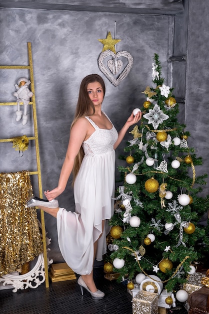 Blonde Frau im weißen Kleid mit Tannenbaum im Studio. neues Jahr 2019