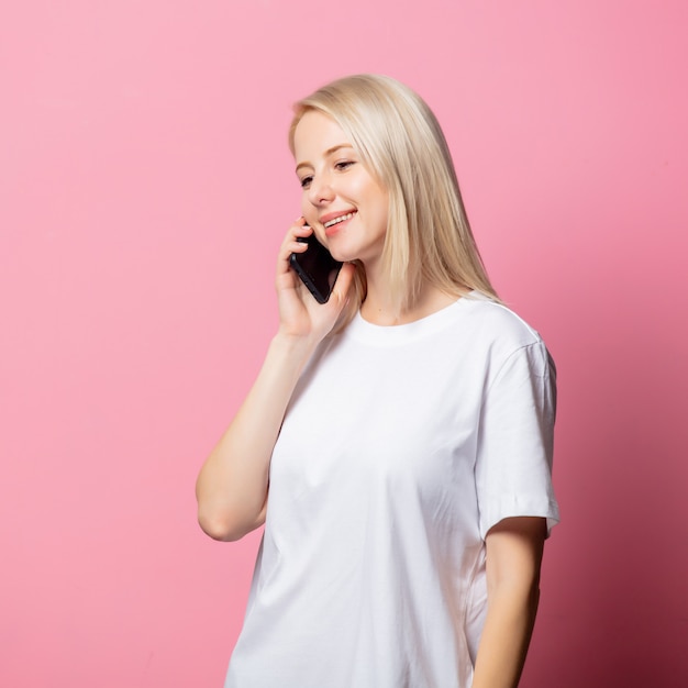 Blonde Frau im weißen T-Shirt mit Handy auf rosa