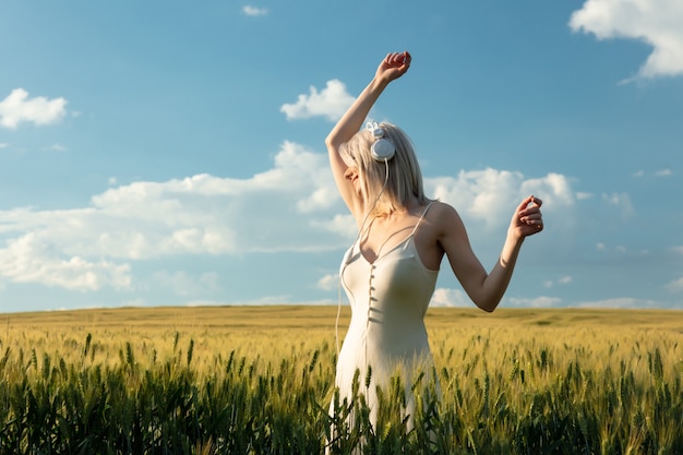 Blonde Frau in den Kopfhörern, die im Weizenfeld in der Sommerzeit tanzen