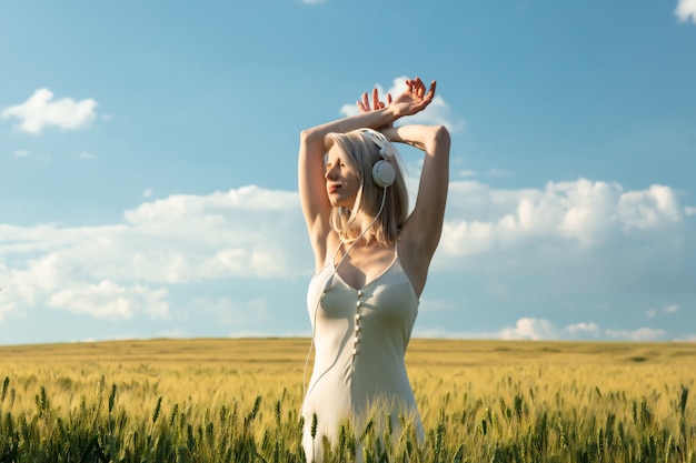 Blonde Frau in den Kopfhörern, die im Weizenfeld in der Sommerzeit tanzen