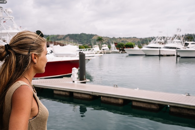 Blonde Frau in einem Hafen mit Blick auf festgemachte Yachten