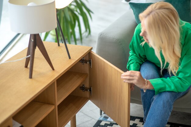 Foto blonde frau in einer grünen bluse, die die schublade öffnet