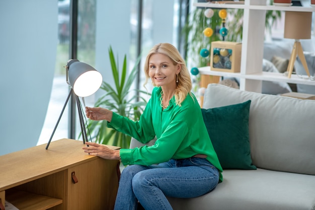Blonde Frau in einer grünen Bluse, die nahe der Lampe sitzt