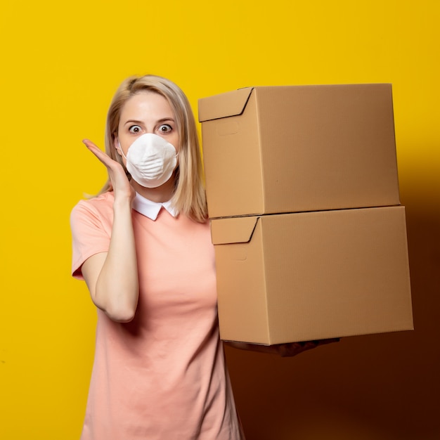 Blonde Frau in Gesichtsmaske mit Lieferboxen auf gelber Wand