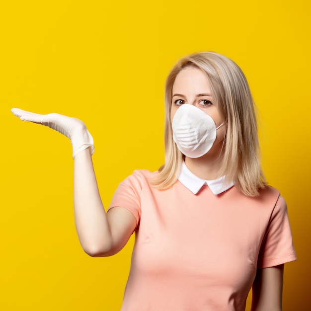 Blonde Frau in Gesichtsmaske und rosa Kleid auf gelber Wand