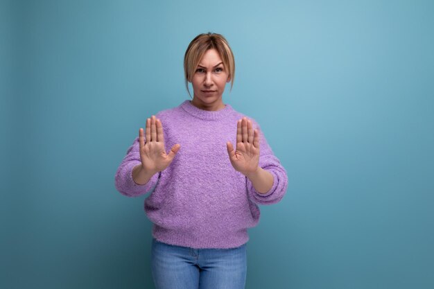 Foto blonde frau in lila kapuzenpullover zeigt stoppschild mit händen auf blauem hintergrund