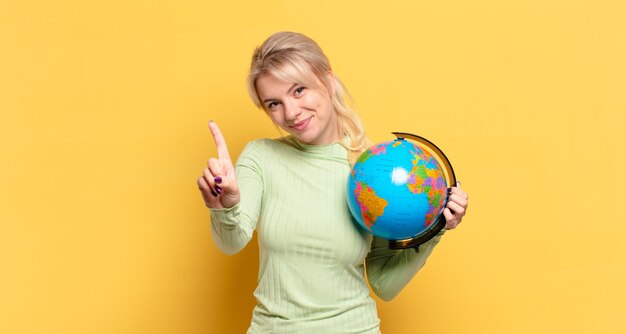 Foto blonde frau lächelt und sieht freundlich aus, zeigt nummer eins oder zuerst mit der hand nach vorne, countdown