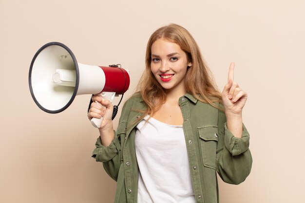 Blonde Frau lächelt und sieht freundlich aus, zeigt Nummer eins oder zuerst mit der Hand nach vorne showing