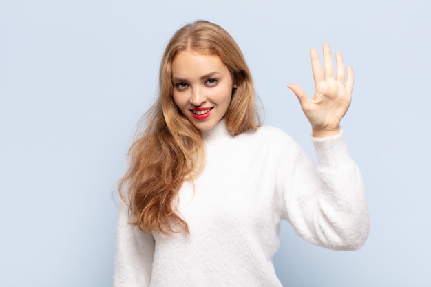 Blonde Frau lächelt und sieht freundlich aus, zeigt Nummer fünf oder fünfte mit der Hand nach vorne, Countdown