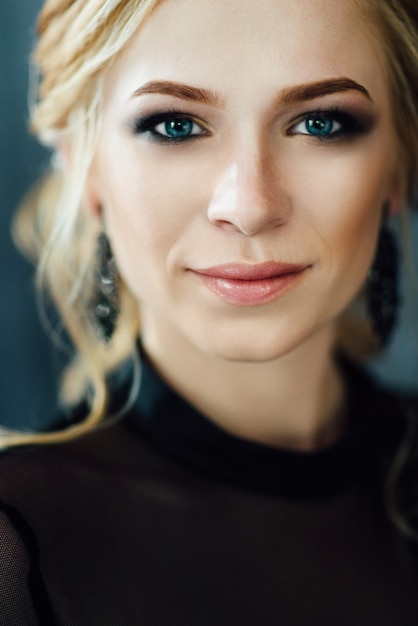 Blonde Frau mit blauen Augen in einem schwarzen Kleid in einem dunkeltürkisen Interieur