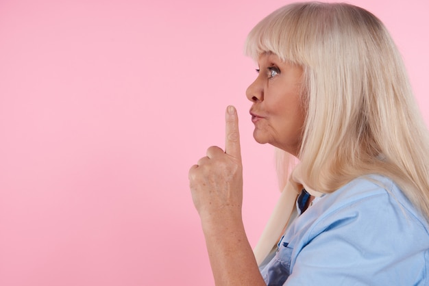 Blonde Frau mit dem Zeigefinger an den Lippen zeigt das leisere Zeichen.