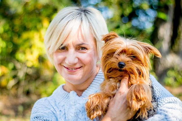 Blonde Frau mit einem magischen Lächeln hält einen kleinen Hund in ihren Armen