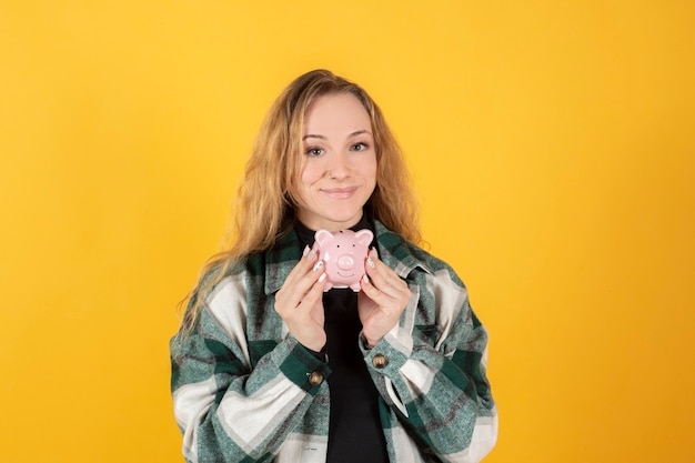 Blonde Frau mit einem Sparschwein, das Geld hineinsteckt