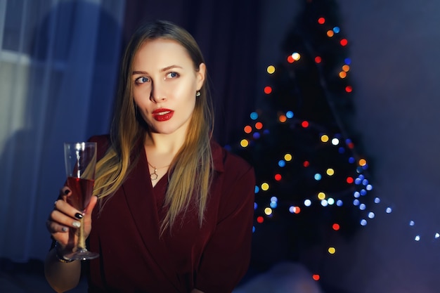 Blonde Frau mit Glas Champagner zu Hause Weihnachtsbaum Neujahrsdekorationen