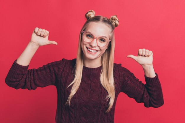 blonde Frau mit Haarknoten und Brille posiert gegen die rote Wand