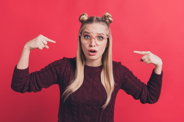 blonde Frau mit Haarknoten und Brille posiert gegen die rote Wand