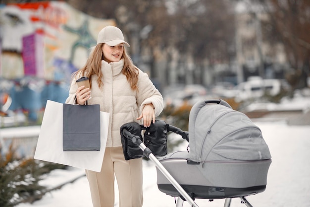 Blonde Frau mit Kinderwagen, die mit Einkaufspaketen in der Stadt spaziert