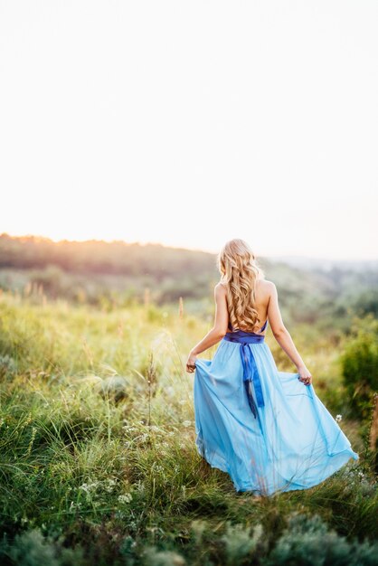 Blonde Frau mit lockerem Haar in einem hellblauen Kleid und einem Mann im Licht des Sonnenuntergangs in der Natur