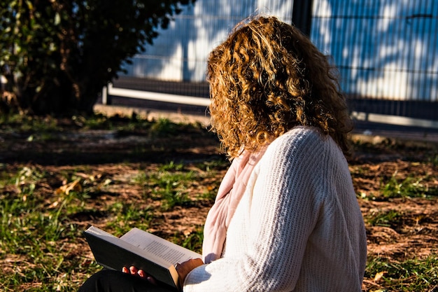 Blonde Frau mit lockigem Haar, die im Park ein Buch liest.