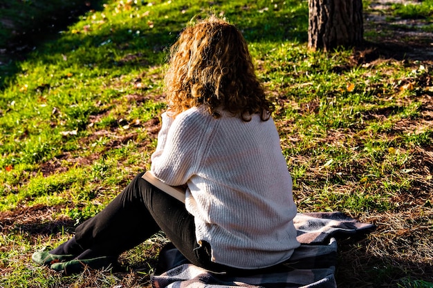 Blonde Frau mit lockigem Haar, die im Park ein Buch liest.