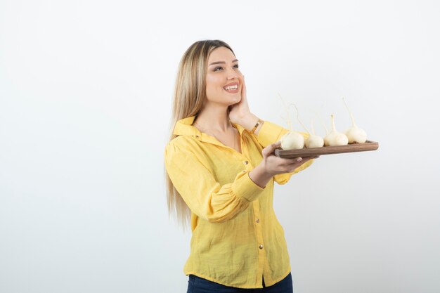 Blonde Frau mit Platte der weißen Rüben, die über Weiß aufwerfen