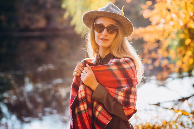 Blonde Frau mit rotem kariertem Schal steht nahe dem See