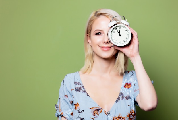 Blonde Frau mit Wecker auf grüner Wand