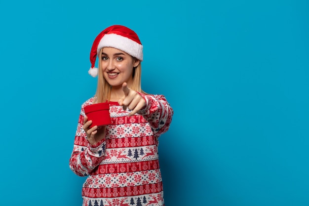 Blonde Frau mit Weihnachtsmütze zeigt mit einem zufriedenen, selbstbewussten, freundlichen Lächeln und wählt Sie