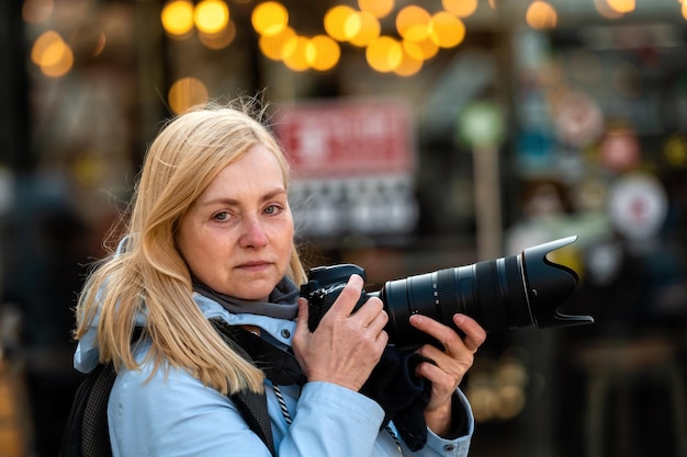 Blonde Frau mittleren Alters mit einer Kamera am Abend auf dem Lifestyle-Konzept der Straßen der Stadt