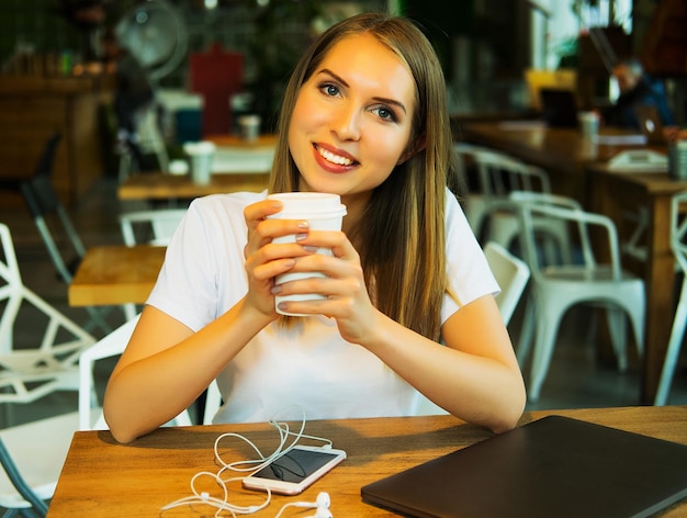 Blonde Frau trinkt Kaffeetee und benutzt Laptop in einem Café