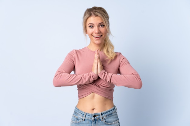 Blonde Frau über isoliertem Blau hält Handfläche zusammen.