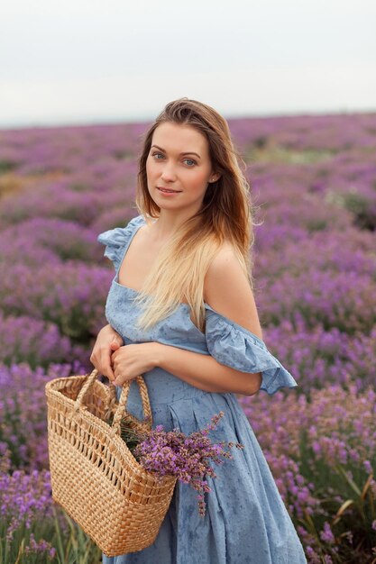 Blonde Frau unter dem Regen auf dem Lavendelfeld Provence. Sammeln von Blumen in die Weidentasche