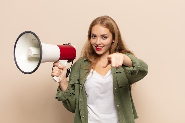 blonde Frau zeigt mit einem zufriedenen, selbstbewussten, freundlichen Lächeln und wählt dich