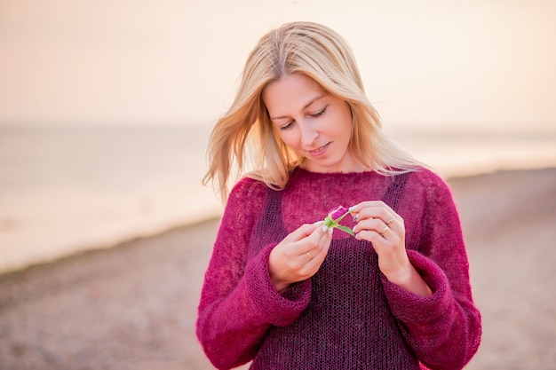 Blonde Frauen im Freien, die bei Sonnenuntergang auf dem Sand in Richtung Meer gehen