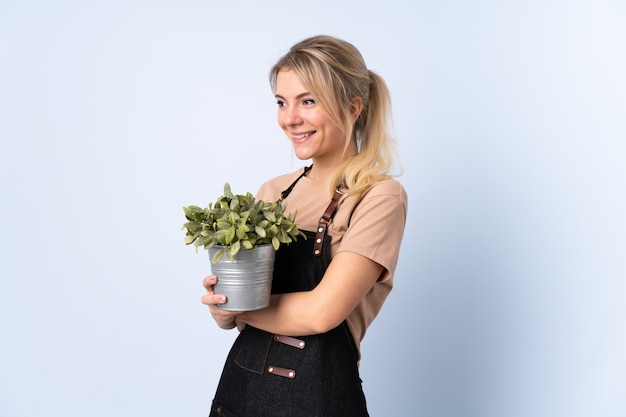 Blonde Gärtnerfrau, die eine Pflanze über lokalisiertem Blick zur Seite hält